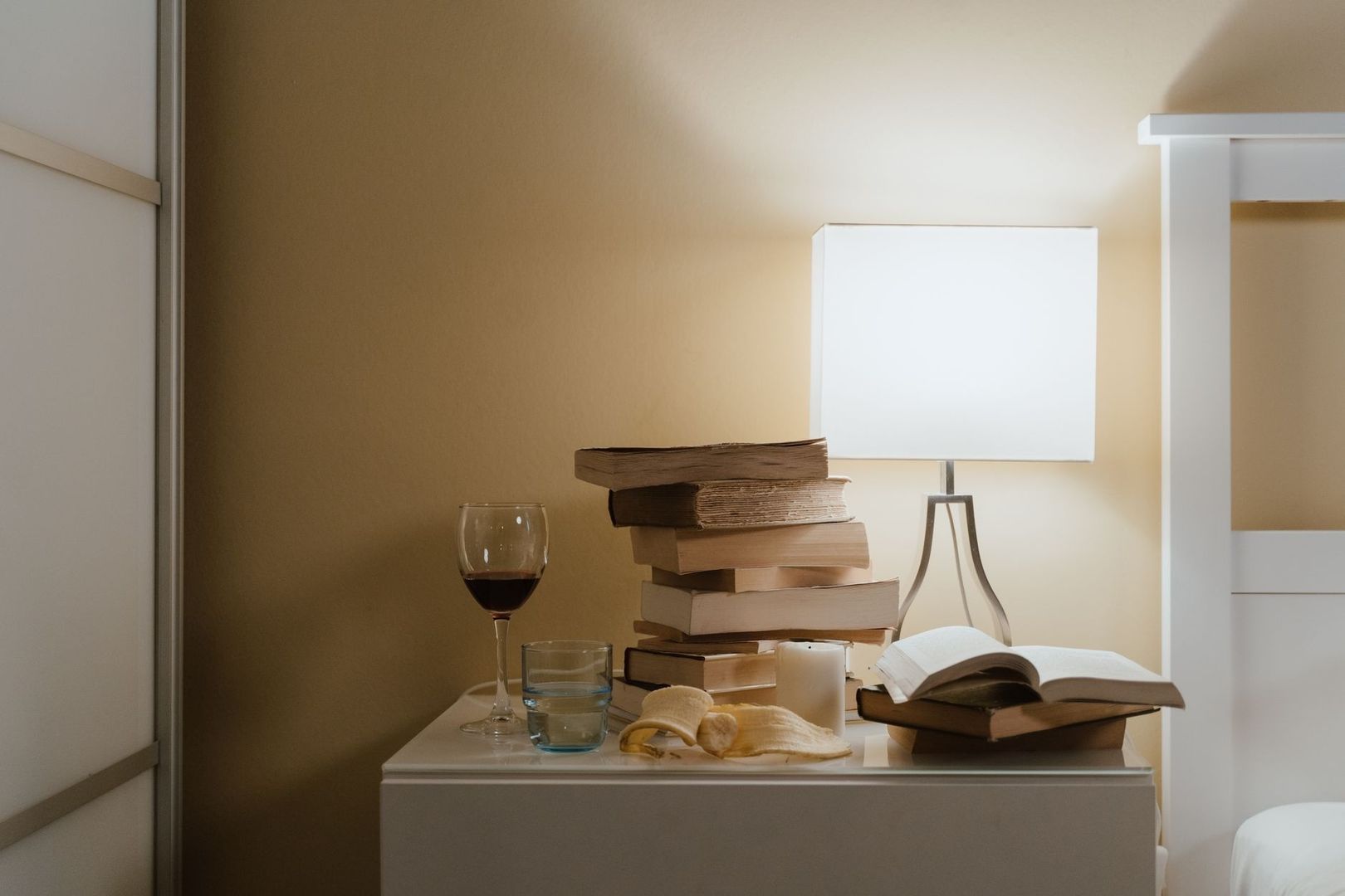 Abendliche Leseszene mit Büchern, Wein, Wasser und leuchtender Lampe